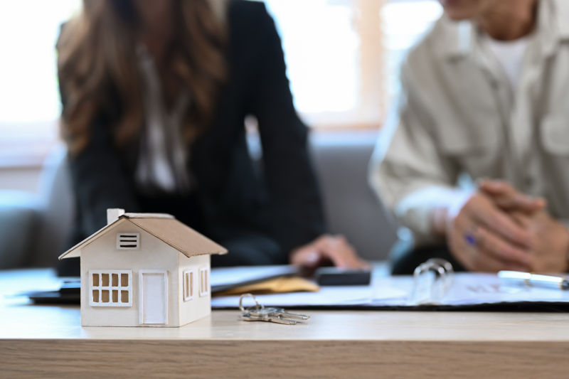 House model on wooden table and  financial adviser consulting contract mortgage loan with elderly man in background.